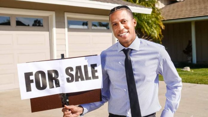 A real estate agent holding a “for sale” sign in front of a house