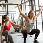 Personal trainer guiding woman doing barbell squats at gym